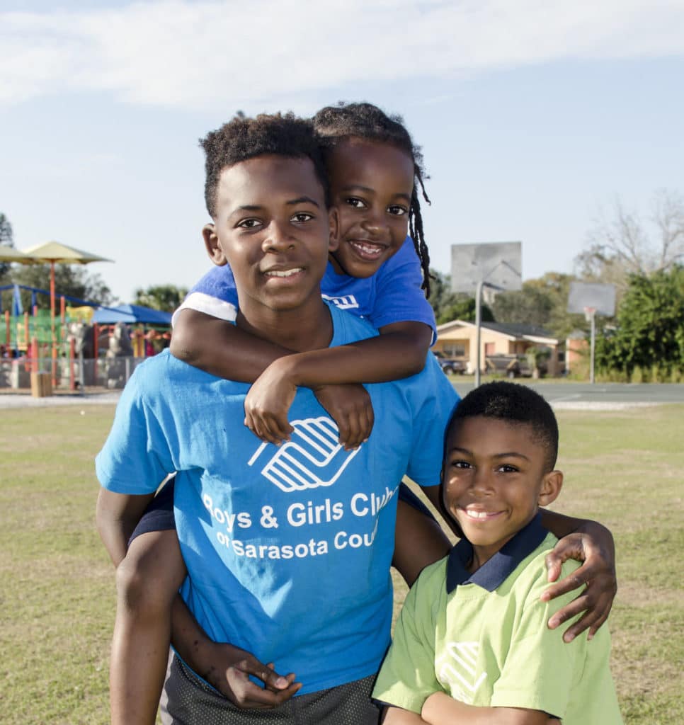 A group of three kids, one older and two younger on a soccer field with boys and girls club shirts on