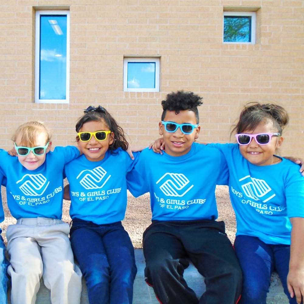 A group of four kids wearing sunglasses and boys & girls club TV shirts