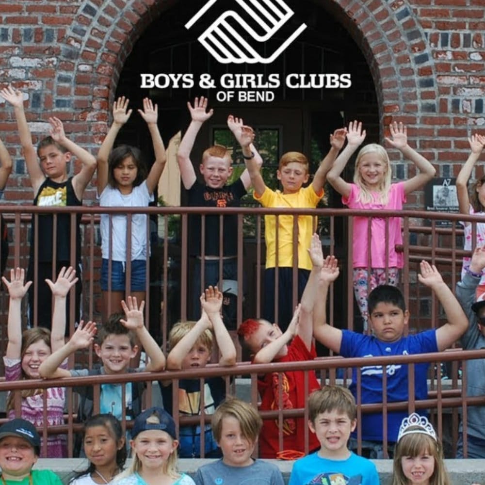 A group of kids standing in front of the Boys & Girls Clubs of bend with their arms up in enjoyment.