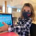 A picture of a young girl with a mask and a touchscreen pad showing the camera