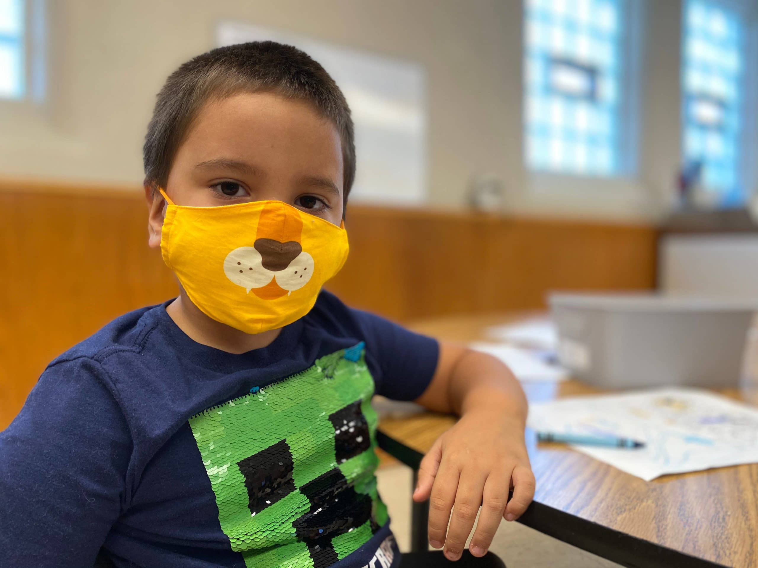 a young boy in a classroom wearing a mask