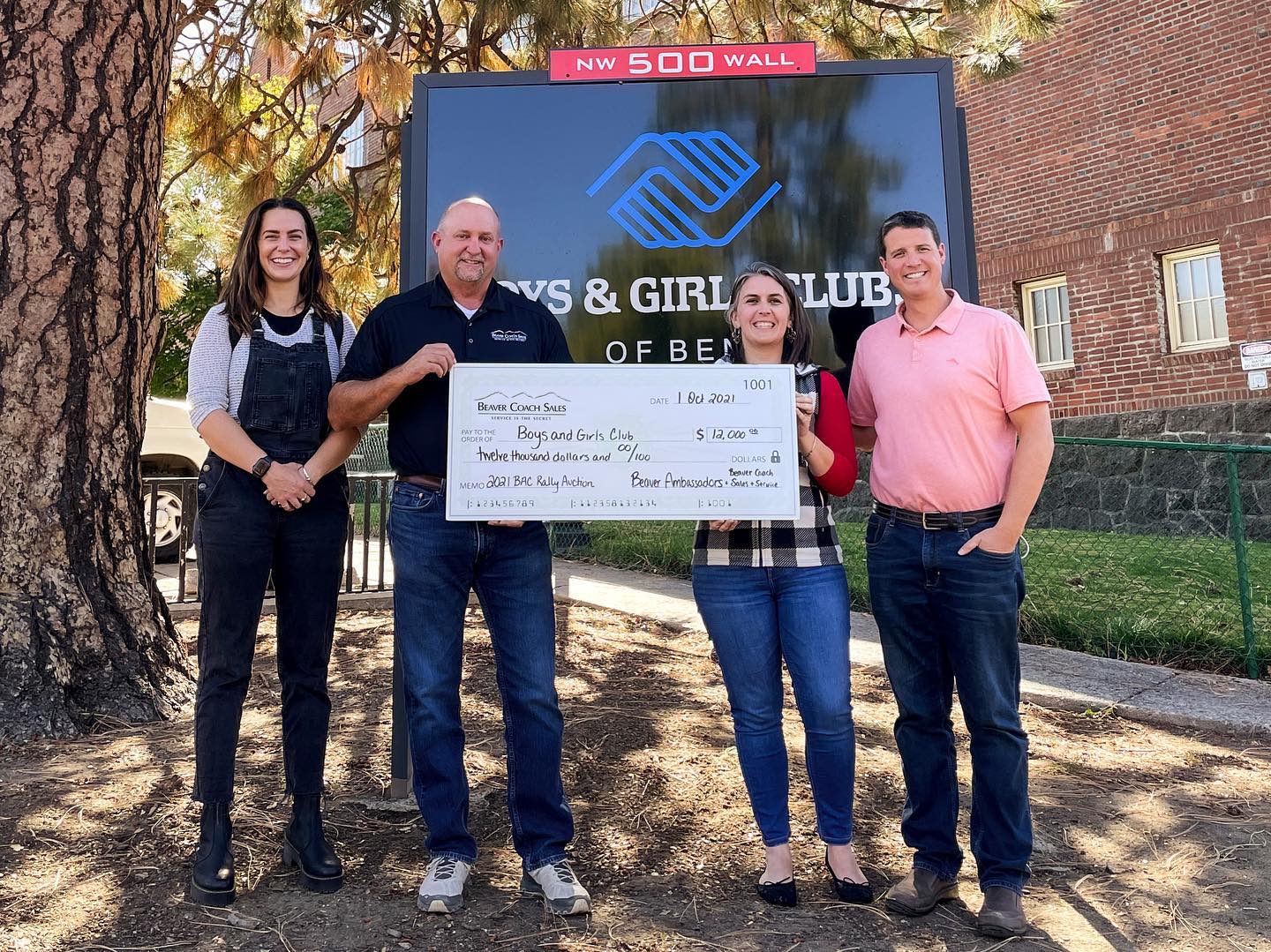 Four people standing with a large check in front of the boys & girls club sign