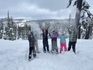 kids on top of a mountain in snow suits throwing snow in the air