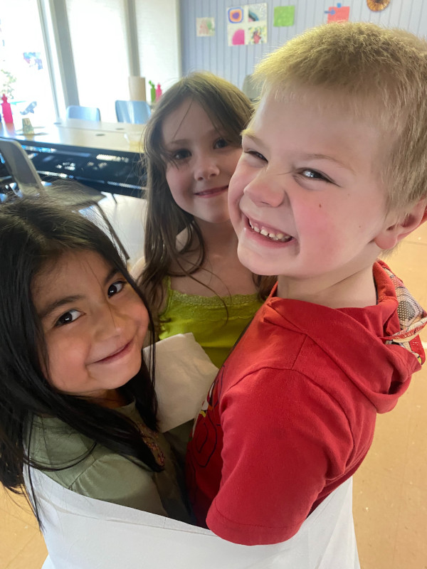 Three kids in a classroom playing a game wrapped together in a fabric