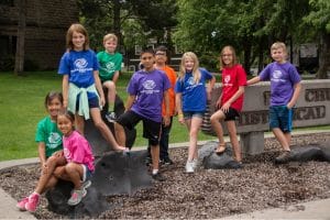 A group of kids sitting on a sign in a park with boys & girls club shirts on