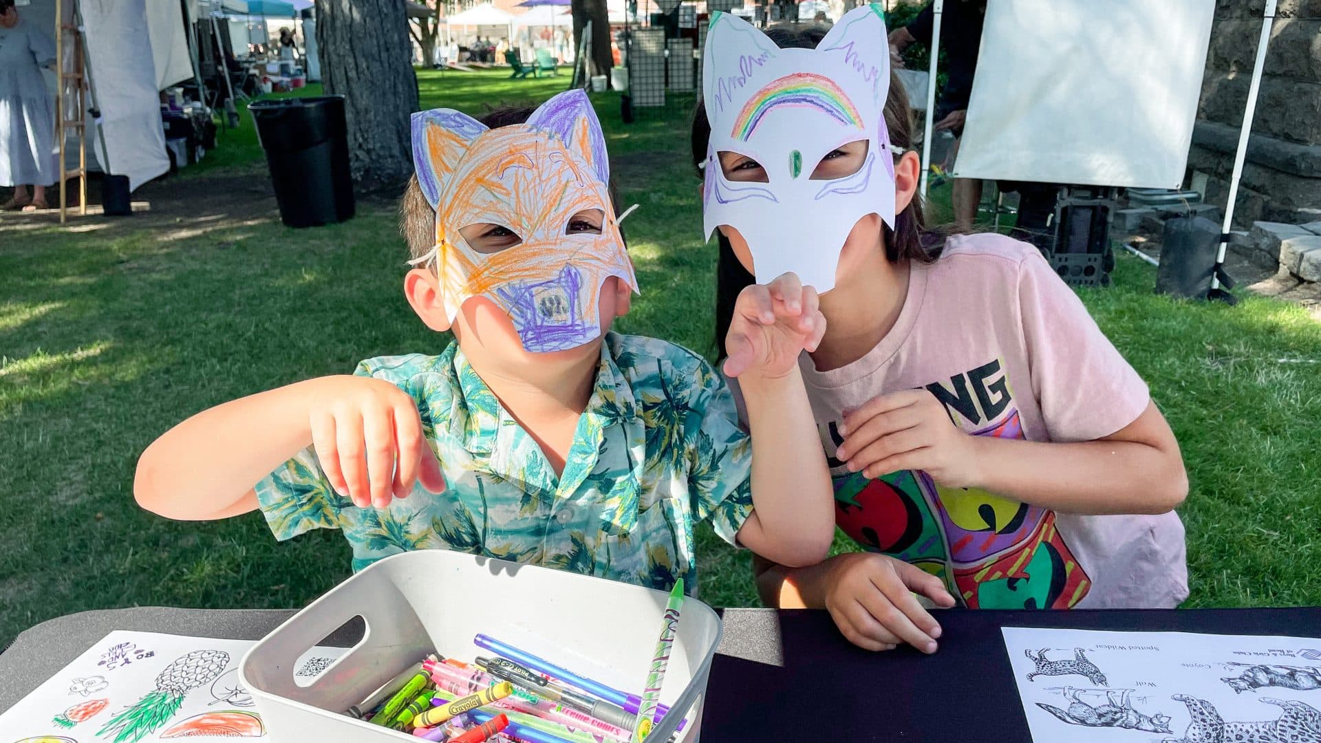 Two kids wearing hand colored animal masks at an event