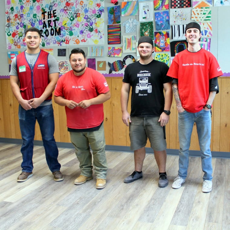 A group of four men standing in front of a wall with kids crafts