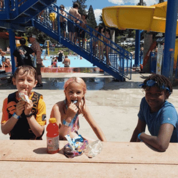 A group of kids sitting in front of a water park eating snacks
