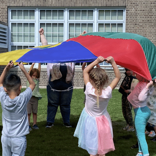 A group of children playing the parachute game with a multicolored parachute.