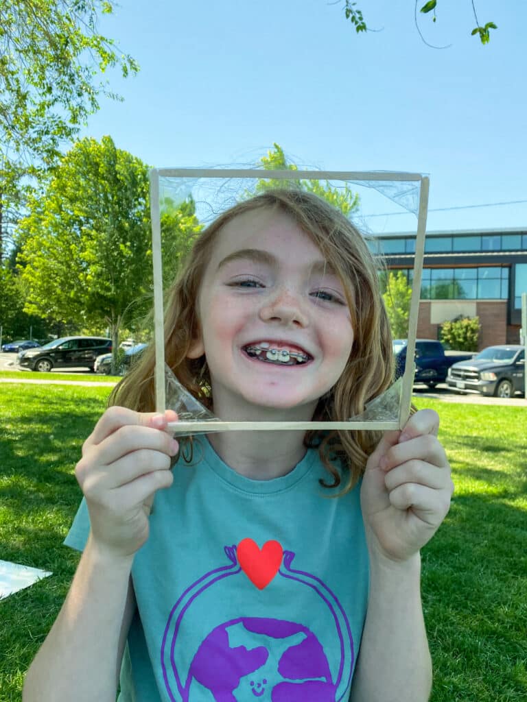 a girl holding a frame around her face and smiling at the camera
