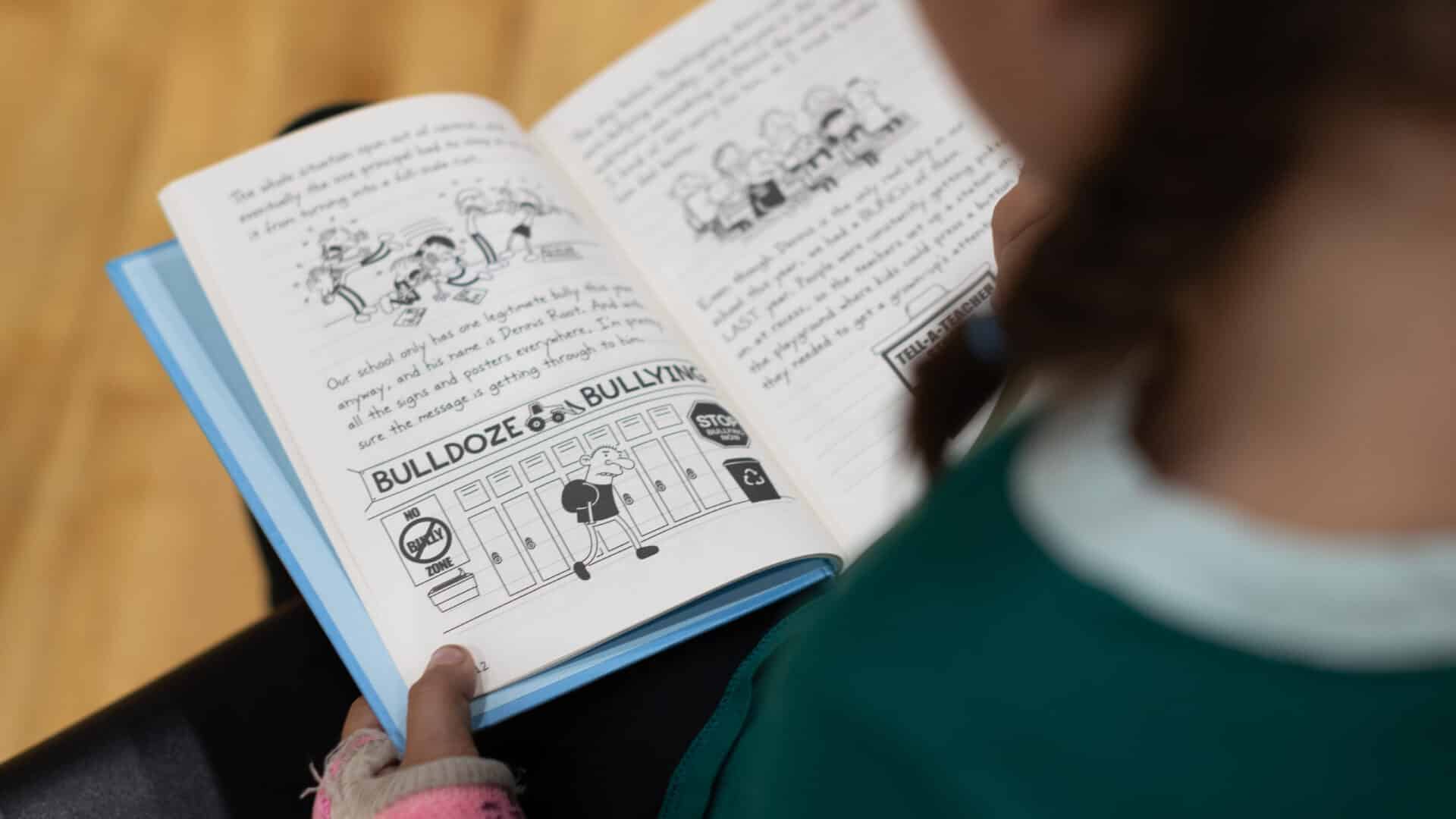 A young child reading a book while sitting on a wooden floor