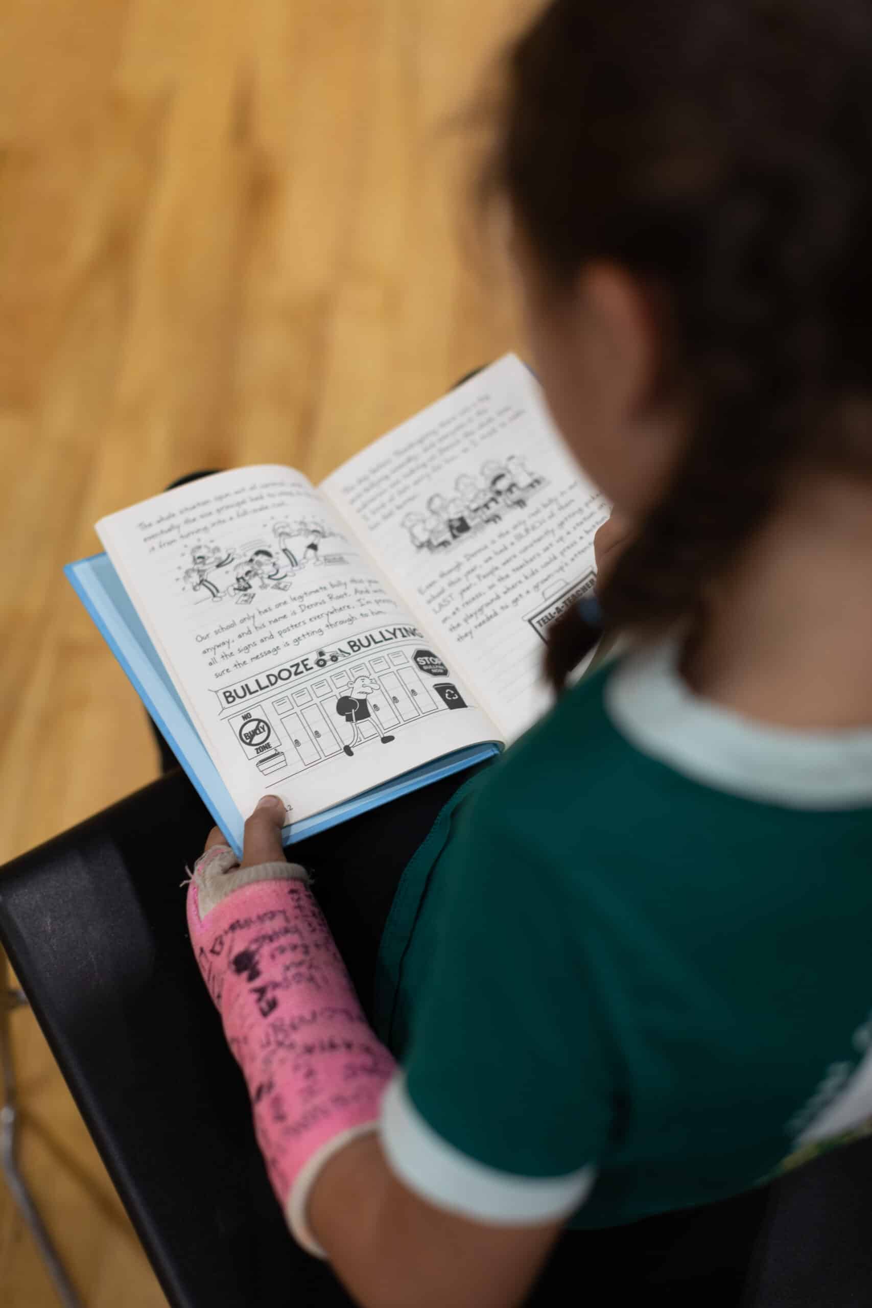 A young child reading a book while sitting on a wooden floor