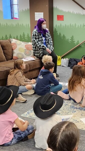 A group of kids sitting criss-cross in a classroom listening to a teacher 