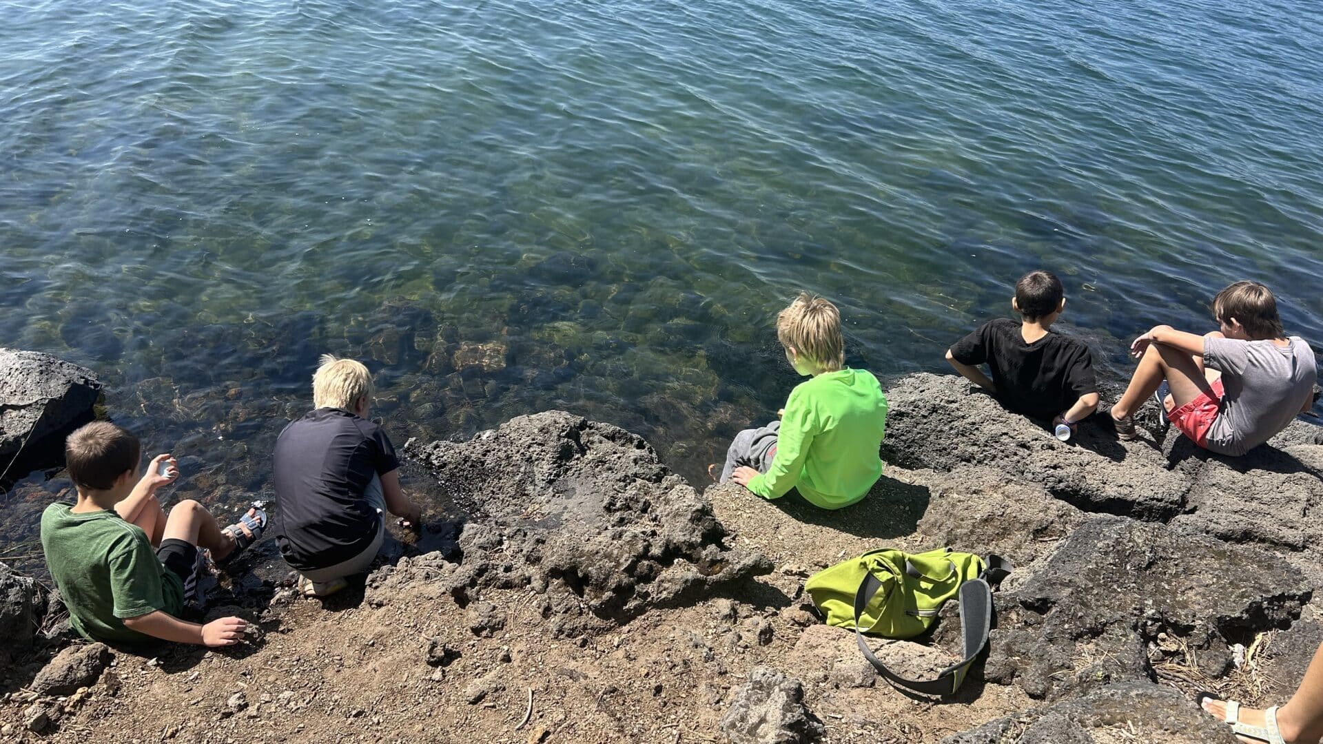 A group of children sitting on the side of a lake