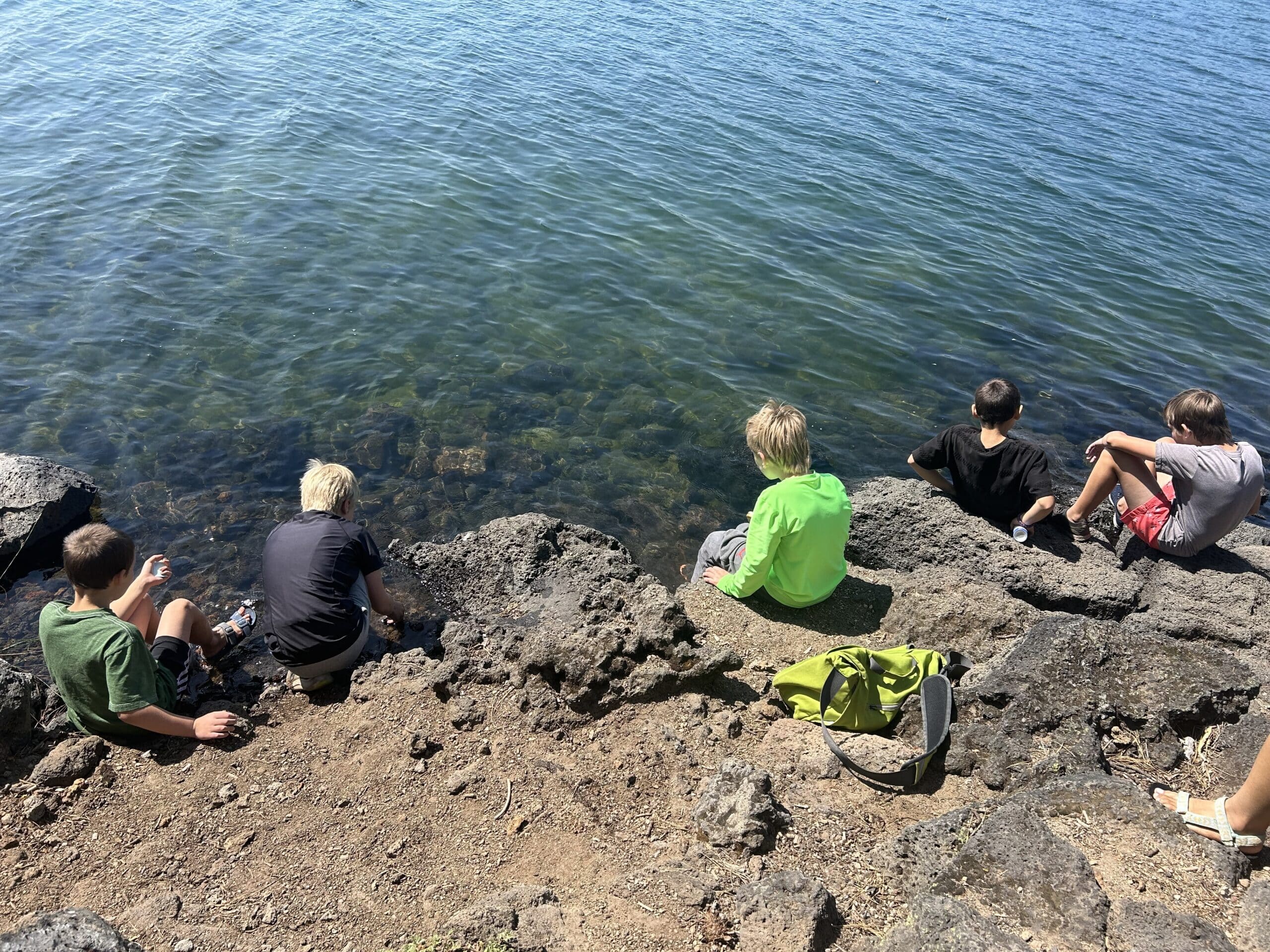 A group of children sitting on the side of a lake