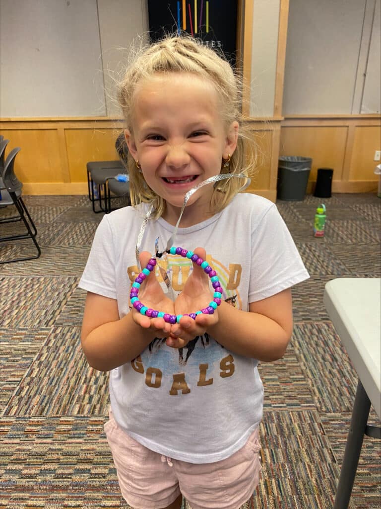 A young girl holding up a hand made bracelet